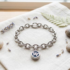 May include: A silver-toned chain link bracelet featuring a circular pendant. The pendant has a dark blue centre with a white butterfly cutout design. The bracelet is constructed with thick, rounded metal links and a secure circular clasp mechanism.