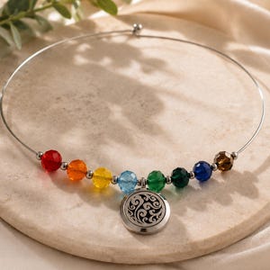 May include: A silver-toned wire choker necklace featuring a series of faceted, multi-coloured beads in red, orange, yellow, light blue, green, dark green, dark blue, and brown, centred with a round, silver-toned metal pendant with a cut-out swirl design.