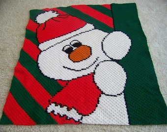 May include: A crocheted snowman blanket with a red and green striped background. The snowman is wearing a red hat and scarf.