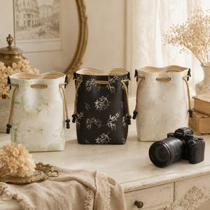 May include: Three cylindrical drawstring bags with a soft interior lining. One bag is light green with a subtle pattern, one is black with a white bamboo leaf print, and one is off-white with a delicate, light-colored bamboo leaf pattern.