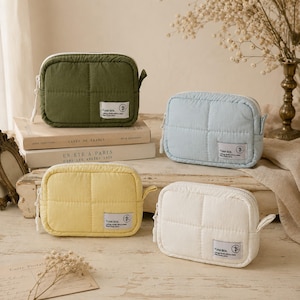 May include: Four rectangular quilted pouches in olive green, light blue, pale yellow, and white. Each pouch features a white zip, a side tab, and a rectangular fabric label with the text YUAN BEN and a circular logo with a cross symbol.