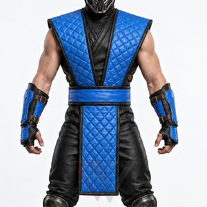 Könnte beinhalten: Ein Kostüm bestehend aus einer schwarz-blauen gesteppten Weste mit passendem blauem Gürtel und einem langen blauen gesteppten Tabard. Das Outfit umfasst schwarz-blaue Unterarmschoner mit braunen Lederriemen und Schnallen, getragen über einer schwarzen Hose.