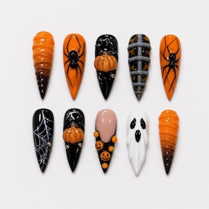 May include: A set of ten stiletto-shaped press-on nails featuring Halloween designs. The collection includes orange and black ombre, black with spiders, 3D pumpkins, grey cage patterns, white spiderwebs, a ghost figure, and small orange jack-o'-lanterns.