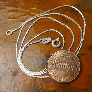 May include: A silver chain necklace with a lobster clasp. The chain is laid out on a brown surface next to a US penny.