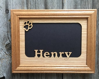 May include: A wooden picture frame with a black background and a cutout paw print in the top corner. The name "Henry" is cut out of the wood below the paw print.