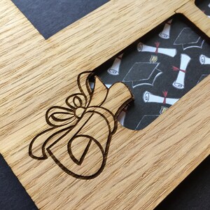 Peut inclure: Cadre photo en bois sur le th&egrave;me de la remise de dipl&ocirc;mes, avec un motif de dipl&ocirc;me et de n&oelig;ud grav&eacute; au laser. Le cadre comporte des ouvertures pour plusieurs photos, avec un fond &agrave; motifs de chapeaux et de dipl&ocirc;mes de fin d'&eacute;tudes.