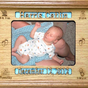 May include: A wooden photo frame with a blue background and the name "Harris Catlin" engraved on it. The frame also includes the baby's birth date, time, weight, and length. The photo shows a newborn baby sleeping in a person's arms.