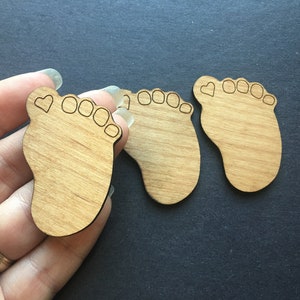 Può includere: Tre forme di piedi di bambino in legno non finito con un piccolo cuore intagliato nell'alluce di ogni piede.