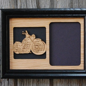 May include: A black rectangular frame containing a light wood panel with two cutouts. The left cutout features a laser-cut wooden motorcycle silhouette with detailed engine and wheel engravings, while the right cutout remains empty with a black backing.