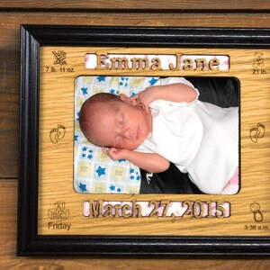 May include: A wooden photo frame with a black border, featuring a baby girl sleeping in a white onesie. The frame includes the baby's name "Emma Jane", birth date "March 27, 2015", and birth stats: 7 lb. 11 oz. and 21 in.