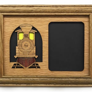 Op de afbeelding: Een houten fotolijst met een uitsnijding van een vintage stoomlocomotief. De lijst heeft een zwarte passe-partout en een enkele foto-opening.