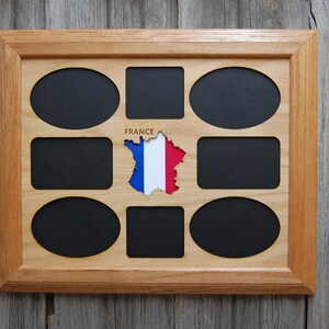 May include: A wooden picture frame with nine oval and rectangular openings for photos. The frame is made of light brown wood and has a dark brown mat. The center opening features a cutout of the country of France with the French flag colors. The text "FRANCE" is printed above the cutout.