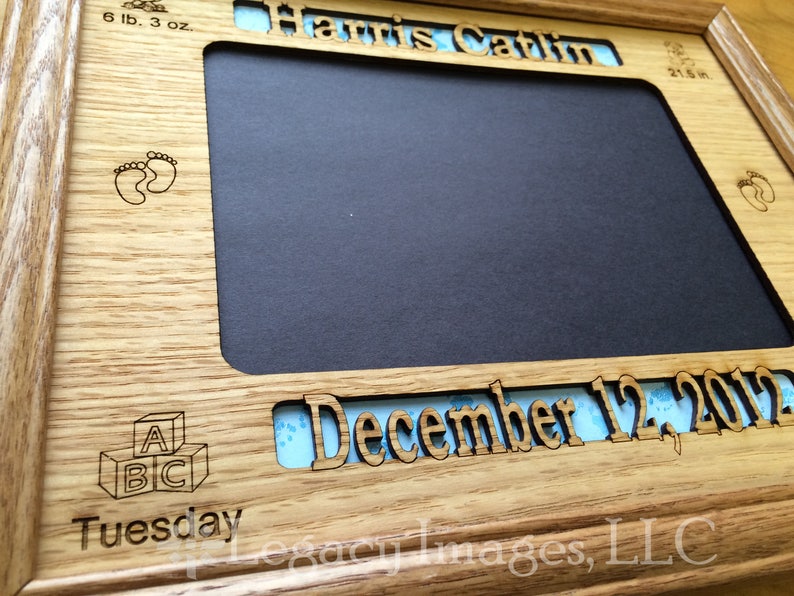 May include: A wooden picture frame with a blue and white patterned mat. The frame is engraved with the text "Harris Catlin", "December 12, 2017", "Tuesday", "6 lb. 3 oz.", "21.5 in", and "A B C".