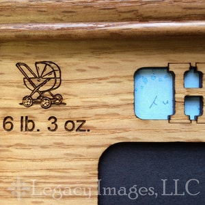 May include: A wooden picture frame with a cutout for a baby's footprint or handprint. The frame is engraved with a baby carriage, the text "6 lb. 3 oz.", and the letter "H".