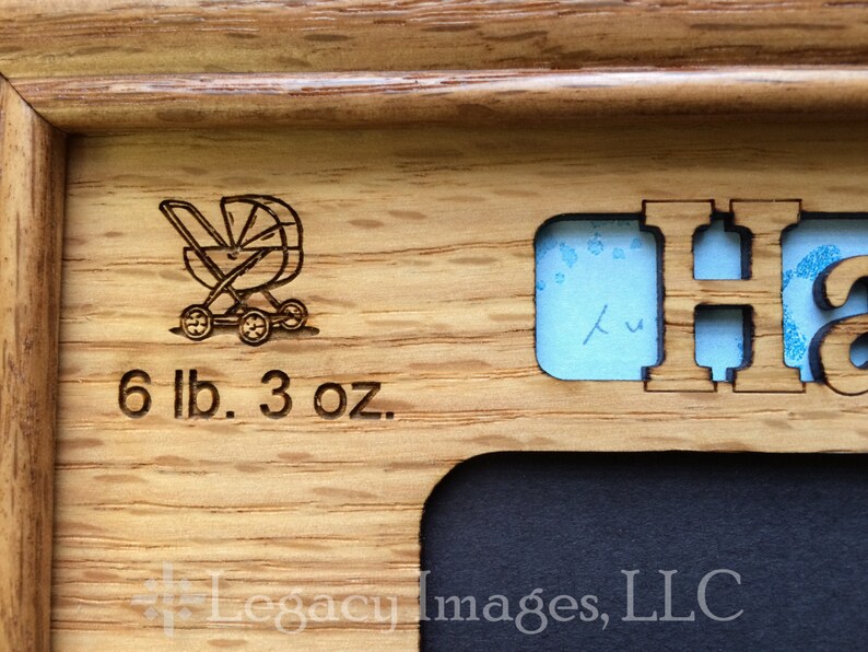 May include: A wooden picture frame with a cutout for a baby's footprint or handprint. The frame is engraved with a baby carriage, the text "6 lb. 3 oz.", and the letter "H".