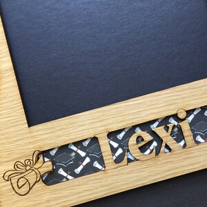 Peut inclure: Cadre photo de graduation en bois avec le nom "Lexi" d&eacute;coup&eacute;. Le cadre comporte des espaces pour une photo et une zone circulaire. Le nom est rempli d'un motif de chapeau de graduation et de dipl&ocirc;me. Un dessin de dipl&ocirc;me est grav&eacute; sur le cadre.