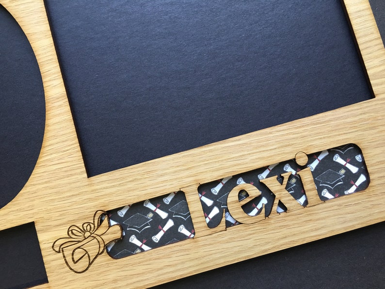 Peut inclure: Cadre photo de graduation en bois avec le nom "Lexi" d&eacute;coup&eacute;. Le cadre comporte des espaces pour une photo et une zone circulaire. Le nom est rempli d'un motif de chapeau de graduation et de dipl&ocirc;me. Un dessin de dipl&ocirc;me est grav&eacute; sur le cadre.