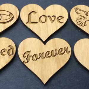 May include: Six light brown wooden heart-shaped cutouts arranged in two rows. The top row features engraved images of two interlocking rings, the word Love, and two doves. The bottom row features the words Blessed, Forever, and the letter S.