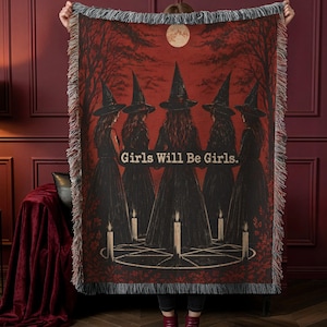 May include: A rectangular woven throw blanket featuring a dark red and black scene of five figures in pointed hats standing in a circle with candles and a pentagram. The text Girls Will Be Girls is printed in the center. The edges have fringe.
