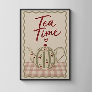 Op de afbeelding: Een ingelijste wandkunstprint met een crèmekleurige achtergrond en een geschulpte rand. De tekst Tea Time staat in rood schrift boven een klein rood hartje. Een ronde theepot met groene strepen en rode kersenillustraties staat op een roze vichykleed.