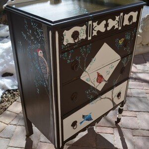 May include: A dark brown dresser with white accents and painted birds. The dresser has four drawers with white fronts and brown trim. The drawers are decorated with painted birds and branches.