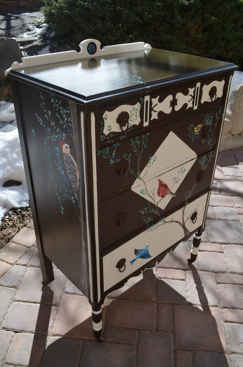 May include: A dark brown dresser with white accents and painted birds. The dresser has four drawers with white fronts and brown trim. The drawers are decorated with painted birds and branches.