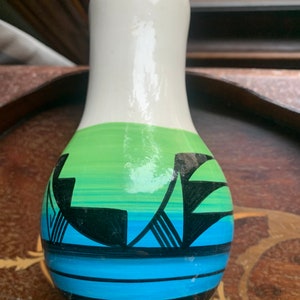 May include: A white ceramic vase with a green, blue, and black geometric design. The vase has a rounded bottom and a narrow neck.