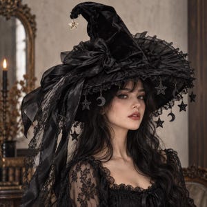 May include: A black velvet pointed hat featuring a wide, ruffled brim adorned with hanging silver-toned star and crescent moon charms. The hat includes a large black satin ribbon bow and delicate lace trim, with a single star charm at the tip.