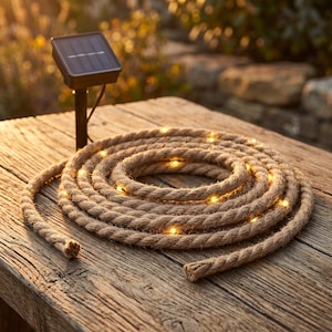May include: A coiled length of thick, natural-colored jute rope embedded with small, glowing warm white LED lights. The rope is connected to a black rectangular solar panel mounted on a short stake, designed for outdoor illumination.