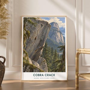 May include: A vertical rectangular art print in a light wood frame featuring a landscape illustration of the Cobra Crack rock formation in Squamish, British Columbia, Canada. The print displays a climber on a granite cliff with pine trees.