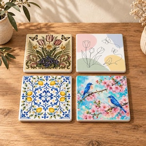 Puede incluir: Cuatro posavasos cuadrados con diseños distintos: uno con un arreglo floral botánico detallado, uno con arte lineal minimalista de tulipanes y mariposas, uno con un patrón de limones azul y amarillo, y uno con dos pájaros azules sobre flores de cerezo.
