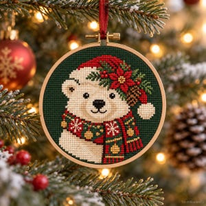 May include: A circular embroidery hoop containing a cross-stitch pattern of a polar bear wearing a red Santa hat adorned with a poinsettia and pinecone. The bear wears a red and green scarf with snowflake and ornament patterns on a dark green background.