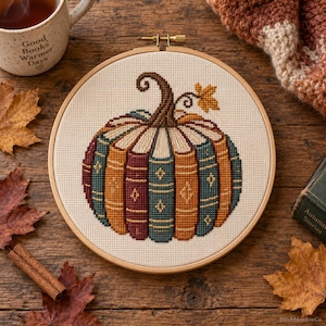 Puede incluir: Un bastidor de bordado circular de madera que contiene un diseño de punto de cruz de una calabaza construida con lomos de libros verticales en tonos naranja, verde azulado y rojo oscuro, rematada con un tallo marrón y una hoja amarilla.