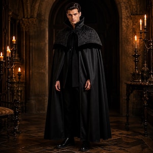 May include: A floor-length black cape featuring a high standing collar and a decorative dark floral brocade pattern across the shoulders. The garment is constructed with a smooth, solid black fabric base and a velvet-textured trim along the yoke.