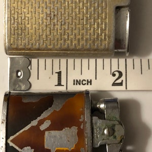 May include: Two vintage lighters, one with a silver finish and a geometric pattern, the other with a brown and silver finish and a geometric pattern. The lighters are about 1 inch in length.