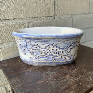 Peut inclure: Un pot en céramique blanche avec un motif de dragon bleu et blanc. Le pot est de forme ovale et a une finition lisse et émaillée.