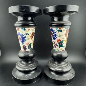 May include: A pair of black wooden candle holders with a white base and colorful floral designs.