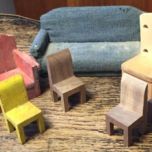 May include: A collection of miniature wooden furniture, including a red armchair, a yellow chair, a blue sofa, and several small wooden chairs. The furniture is arranged on a wooden surface, showcasing a rustic aesthetic.