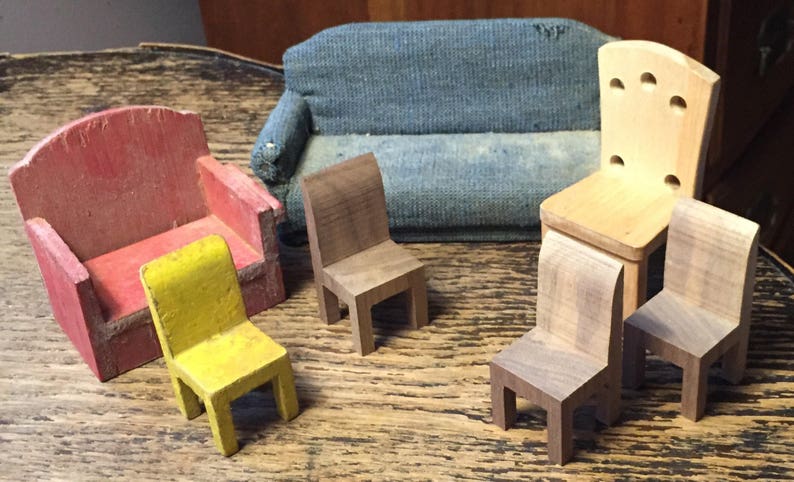 May include: A collection of miniature wooden furniture, including a red armchair, a yellow chair, a blue sofa, and several small wooden chairs. The furniture is arranged on a wooden surface, showcasing a rustic aesthetic.
