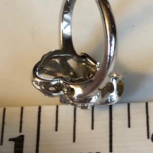 May include: A silver ring with a floral design. The ring is about 1 inch in diameter.