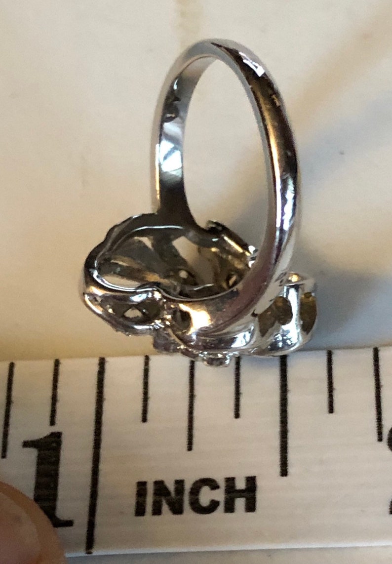 May include: A silver ring with a floral design. The ring is about 1 inch in diameter.