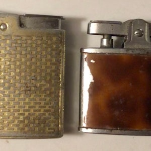 May include: Two vintage lighters, one with a gold-toned, textured finish and the other with a brown, mottled finish.
