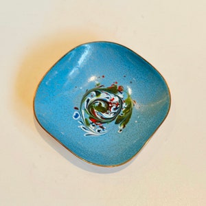 May include: A small, square, blue enamel trinket dish with a gold rim. The dish has a swirling, abstract design in white, green, red, and blue.