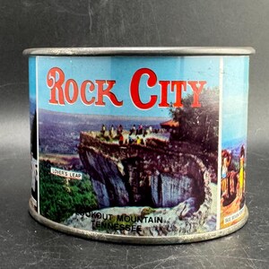 May include: A cylindrical metal souvenir tin featuring a colorful graphic of Rock City on Lookout Mountain, Tennessee. The label displays the text Rock City, Lover's Leap, and Lookout Mountain Tennessee, with a scenic view of a rocky cliffside.
