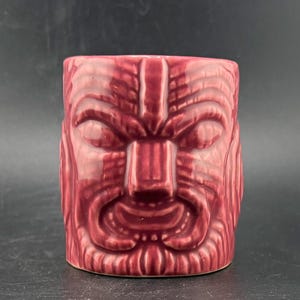 Peut inclure: Un mug tiki en céramique marron avec un motif de visage sculpté détaillé. Le mug a une forme rectangulaire avec une large ouverture et une surface texturée, parfait pour les boissons tropicales.
