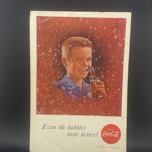 May include: Vintage Coca-Cola advertisement featuring a smiling young person holding a bottle of Coca-Cola. The ad has a red background with bubbles and the text "Even the bubbles taste better!" The Coca-Cola logo is visible.