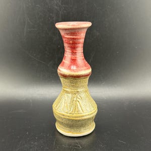 Puede incluir: Un pequeño jarrón de cerámica con un esmalte rojo y marrón. El jarrón tiene un cuello estrecho y una base ancha.