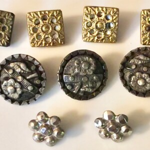 May include: Assortment of vintage buttons in gold and silver tones. The buttons feature various designs, including floral, geometric, and ornate patterns.