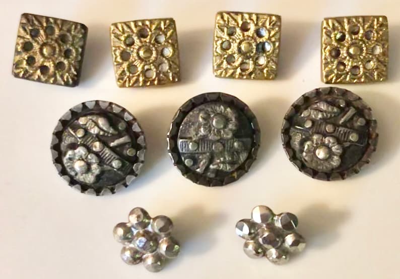 May include: Assortment of vintage buttons in gold and silver tones. The buttons feature various designs, including floral, geometric, and ornate patterns.