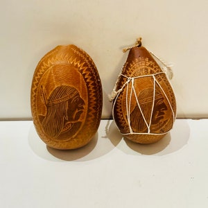 May include: Two intricately carved gourds, one with a white string design and the other with a carved image of a person wearing a headdress.